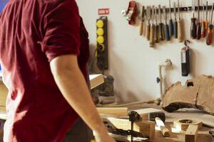 artesano trabajando en estudio utilizando lijado bloquear a eliminar imperfecciones en madera pedazo. creativo persona disfrutando bricolaje pasatiempo, utilizando grueso grado papel de lija a hacer manual lijado en Tablas de madera foto