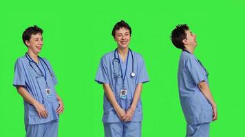 Cheerful smiling medical assistant standing against greenscreen backdrop, feeling confident and successful while she wears hospital scrubs. Nurse surgeon works in healthcare industry. Camera B. photo