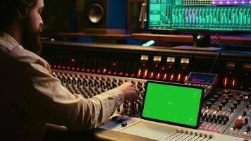 audio experto mezcla y dominar melodías en edición software siguiente a pantalla verde tableta, productor y grabación pistas por emprendedor botones y atenuadores. sonido ingeniero en controlar habitación. cámara b. foto