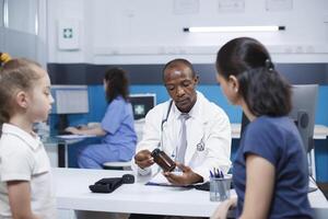 Concerns regarding mother and daughter are discussed with a healthcare expert. While holding a prescription bottle, African American physician describes medication and diagnosis to Caucasian patients. photo