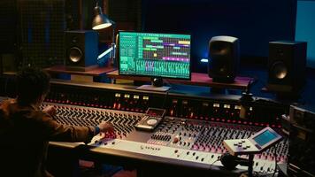 African american audio expert adding sound effects on tracks in post production, operating mixing console and pushing sliders. Producer creating music for his new album, audio mixer. Camera B. photo