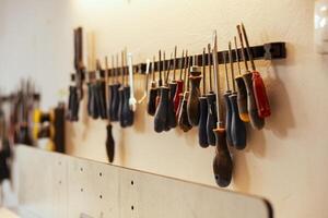 Close up shot of various woodworking tools on rack in workshop used for repairing or creating wooden objects. Chisels, screwdrivers, wrench and pliers on wall in carpentry studio photo