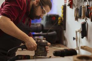 Carpenter wears protective glasses at workbench, using orbital sander with fine sandpaper on lumber to achieve refined finish. Man in assembly shop uses angle grinder on wood for professional results photo