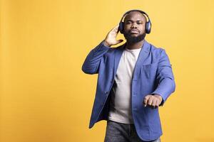 africano americano hombre escuchando a música en inalámbrico estéreo auriculares durante hora apagado. bipoc audiófilo disfrutando canciones en alto fidelidad auriculares, aislado terminado estudio antecedentes foto
