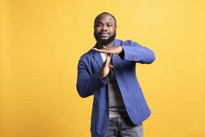 Portrait of smiling african american man asking for timeout, doing hand gestures. BIPOC person doing pause sign gesturing, wishing for break, isolated over studio background photo