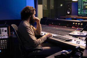 Sound designer mixing and mastering music in recording studio, examines audio digital software on pc before adding effects in post production. Technician works in control room. Close up. photo