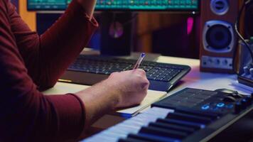 Composer developing an original track In his home studio, writing down lyrics and harmonic notes before recording the song melody. Musician using DAW computer apps for creating music. Camera A. photo