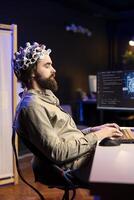 hombre con eeg auriculares en mecanografía en teclado, escritura código permitiendo él a transferir mente dentro computadora virtual mundo. transhumanista clausura ojos, trascendiendo, convirtiéndose uno con ai foto