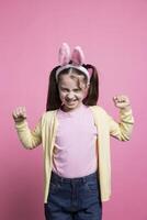 Angry irritated young girl expressing her disappointment in studio, wearing bunny ears buy feeling displeased about something. Little toddler shows her disapproval, negative emotions. photo