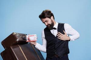 Bellboy with heart condition who works in travel sector, provides cardiac medication to treat sickness. Young hotel staff holding box of pharmaceuticals on camera, showcasing cure. photo