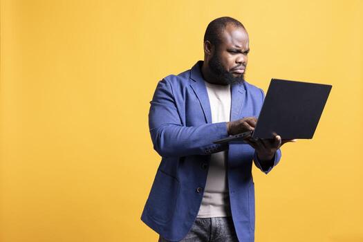Upset man frowning while looking at laptop, dissatisfied with company profits, studio background. Irked employee flabbergasted by low income, doing financial analysis on notebook photo