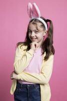 Little schoolgirl thinking about easter presents and celebration, feeling happy and joyful with her bunny ears in front of camera. Young child toddler with lovely pigtails fooling around. photo