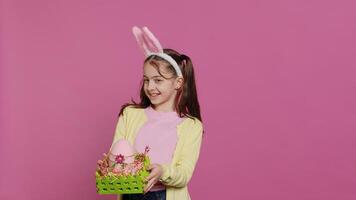 Smiling pleased girl presenting her handcrafted easter basket filled with painted eggs and other festive decorations for holiday celebration. Joyful small kid proud of her arrangement. Camera A. photo