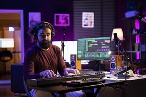 Artist playing piano midi controller and recording new tunes, producing new electronic notes in his home studio. Sound engineer working on digital audio workstation interface, synthesizer keys. photo