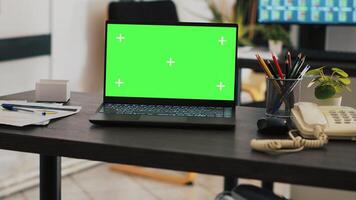 Focus on green screen laptop on office desk with computer in blurry background showing stock exchange data. Close up of mockup notebook and trading platform displayed on PC screen in the back photo