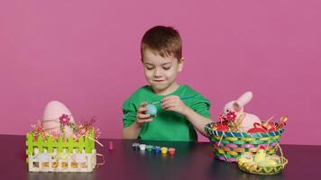 pequeño alegre chico elaboración hecho a mano Pascua de Resurrección decoraciones por pintura con acuarela y pinceles. pequeño joven niño utilizando Arte suministros colorante huevos para día festivo, decorando actividad. cámara una. foto