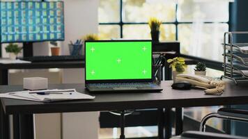 Wheelchair in office offering accessibility to workers with disability and green screen laptop on desk. Mockup notebook in workspace and computer screen in background displaying stock exchange photo