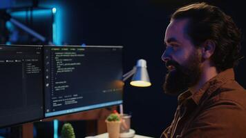 Smiling freelancing developer in home office doing coding on computer at desk. Cheerful IT expert doing contracted job from apartment, writing lines of code at workstation, camera B close up photo