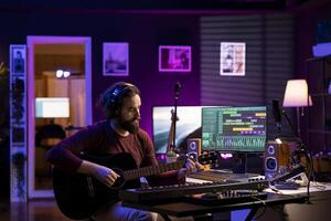 Skilled singer producer recording guitar tunes and adding piano key sounds, creating a beautiful song with mixing console and daw software on pc. Acoustical engineer working with electronic gear. photo