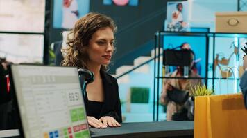 African american retail clerk scanning barcode on bag at cash register, preparing items for customer at department store. Young woman choosing trendy accessories from showroom. Camera A. photo