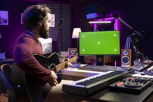 Artist learning to play guitar with internet lessons on greenscreen monitor, watching tutorials for acoustics rehearsal in home studio. Producer learns new string accords for music industry. photo