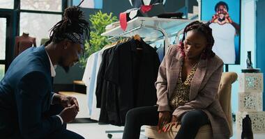 African american store employee helping woman to find the right shoe size, pregnant customer looking to buy comfortable footwear from local shopping center. Client trying on winter boots. Camera B. photo