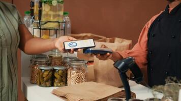 africano americano mujer comprando Fresco bio Produce con nfc móvil pago a posición, secundario sostenible estilo de vida y sano comiendo. comprador mirando para orgánico de cosecha propia frutas y vegetales. foto