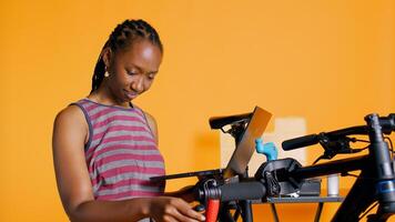 Cheerful mechanic doing bike servicing in studio background atelier shop, looking on laptop maintenance list. Specialist checking online for replacement bicycle parts using notebook, camera B photo