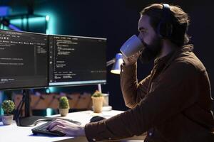 Cybersecurity specialist drinking coffee while looking for company security vulnerabilities and preventing malware infections. Programmer enjoying hot beverage while installing fortified code on PC photo