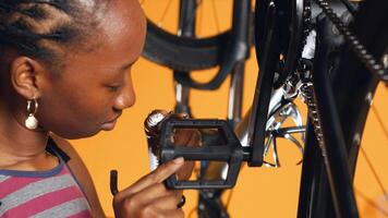 BIPOC employee pushing pedals to spin bike wheel, doing maintenance on it using screwdriver and hex socket wrench, close up. Serviceman dismantling bicycle parts to patch them up, camera A photo