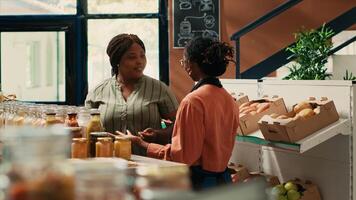 Local storekeeper recommends grains and homemade sauces to loyal customer, ensuring organic source of proteins for goods in jars. Merchant presenting new ecological nonpolluting merchandise. photo