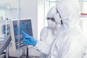 químico en ppe traje explicando a médico vacuna desarrollo en moderno equipado laboratorio señalando en computadora escritorio. doctores examinando virus evolución utilizando alto tecnología investigando diagnóstico en contra covid19 foto