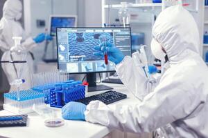 Scientist in scienec lab examining blood test tubes dressed in coverall and face mask. Doctor working with various bacteria and tissue, pharmaceutical research for antibiotics against covid19. photo