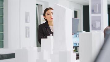 desarrollador trabajando con ordenador portátil a reunir escala elementos, mirando a 3d impreso modelo de edificio maqueta técnico revisando creativo arquitectónico plan para nuevo construcción proyecto. foto