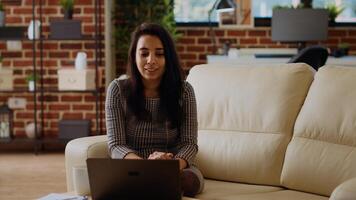 Smiling person excited to catch up with friends during online meeting session while relaxing in modern stylish apartment living room. Woman chatting with mates in videocall using laptop, camera B photo