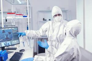 compañeros de trabajo mirando a cada otro vestido en bata traje en contra coronavirus trabajando en vacuna. equipo de doctores trabajando con varios bacterias y tejido, farmacéutico investigación para antibióticos en contra COVID-19. foto