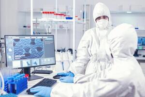 enfermero en proteccion traje que se discute con laboratorio técnico vestido en equipo de doctores trabajando con varios bacterias y tejido, farmacéutico investigación para antibióticos en contra COVID-19. foto