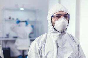 agotado médico equipado con ppe traje durante investigación de vacuna para covid19 en moderno laboratorio. sobrecargado de trabajo investigador vestido en protector traje en contra invección con coronavirus durante global epidemia. foto