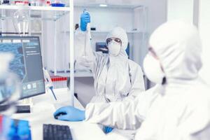 Woman scientist in coverall using micropipette in lab for coronavirus research. Team of microbiologists in research laboratory conducting experiment during global pandemic with covid19. photo