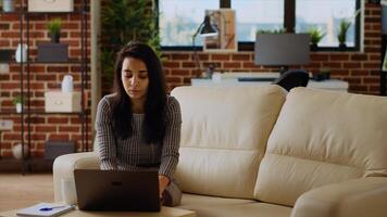 Indian teleworker sitting on couch, focused on finishing tasks in personal office. Remote worker concentrating on correctly inputting data on laptop, hurrying to complete project before deadline photo