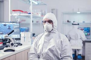 químico sensación cansado desde trabajo para un largo hora en laboratorio sentado a lugar de trabajo. sobrecargado de trabajo investigador vestido en protector traje en contra invección con coronavirus durante global epidemia. foto