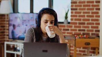 indio mujer Bebiendo café en el Mañana y acecho televisión espectáculo a hogar utilizando auriculares. matinal persona despertar arriba con caliente bebida mientras disfrutando televisión serie en computadora portátil, cámara si foto