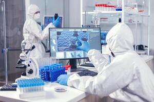 cuidado de la salud doctores investigando evolución de coronavirus trabajando en computadora vestido en mono. laboratorio ingenieros conductible experimentar para vacuna desarrollo en contra covid19 virus foto