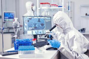 equipo de médico personal vistiendo ppe traje haciendo coronavirus análisis en moderno laboratorio. químico investigador durante global pandemia con covid-19 comprobación muestra en bioquímica laboratorio foto