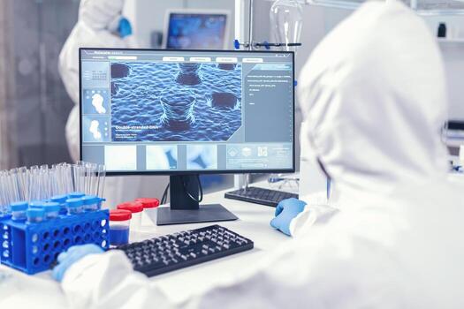 Over the shoulder shot of scientist monitoring and working with coronavirus dressed in ppe. Lab engineers conducting experiment for vaccine development against covid19 virus. photo
