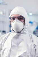 Close up of medicine engineer wearing face mask and suit in laboratory during covid019. Overworked researcher dressed in protective suit against invection with coronavirus during global epidemic. photo