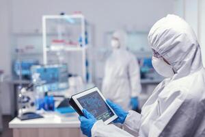 Healthcare researcher analyzing virus on tablet pc during global pandemic on tablet pc. Team of scientists conducting vaccine development using high tech technology for researching treatment against covid19 photo