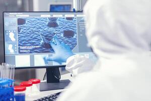 Medical researcher analysing evolution of coronavirus pointing at screen in modern facility dressed in . Lab engineers conducting experiment for vaccine development against covid19 virus photo