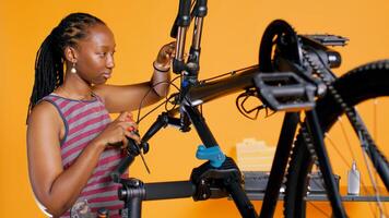 BIPOC technician uses screwdriver to unmount bicycle handlebars, testing components quality in studio background atelier shop. Specialist mechanic unscrewing bike parts in order to mend them, camera B photo