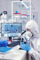 Medic and nurse dressed in ppe equipment checking evolution of coronavirus in laboratory. Scientist in protective suit sitting at workplace using modern medical technology during global epidemic. photo